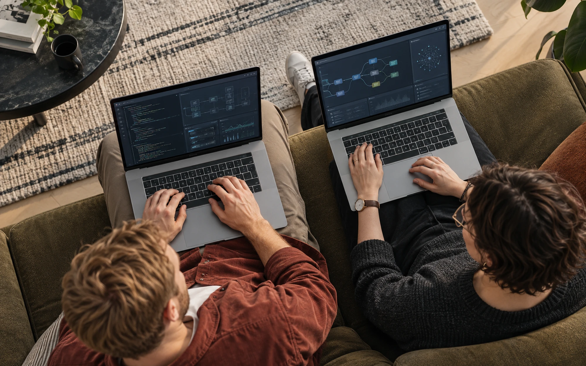 Two colleagues on a sofa working on laptops showing code and system diagrams